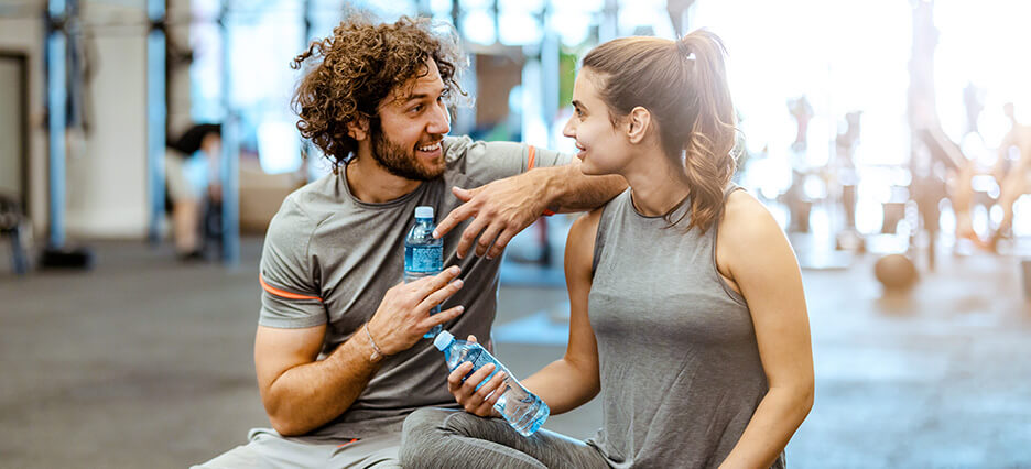 Fitnesstrainer spricht in der Trainingspause mit Sportlerin.