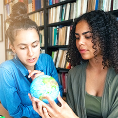 Zwei junge Frauen sehen sich auf einem kleinen Globus die Geografie der Erde an.