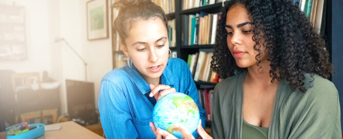 Zwei junge Frauen sehen sich auf einem kleinen Globus die Geografie der Erde an.