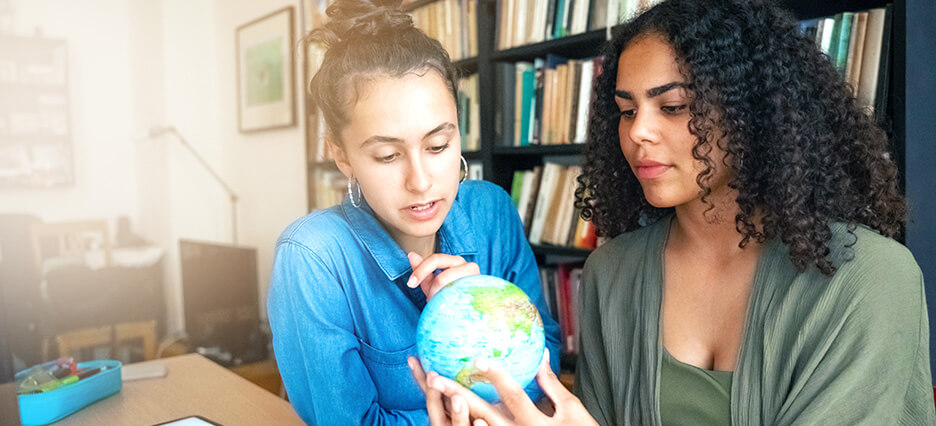 Zwei junge Frauen sehen sich auf einem kleinen Globus die Geografie der Erde an.