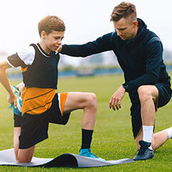 Trainer hilft einem Kind beim Dehnen vor dem Fußballspiel.