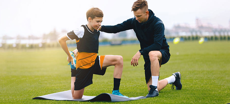 Trainer hilft einem Kind beim Dehnen vor dem Fußballspiel.