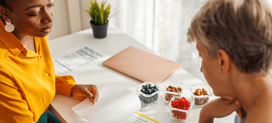 Ernährungsberaterin zeigt Klientin gesunde Snacks und erklärt deren Nährwert.