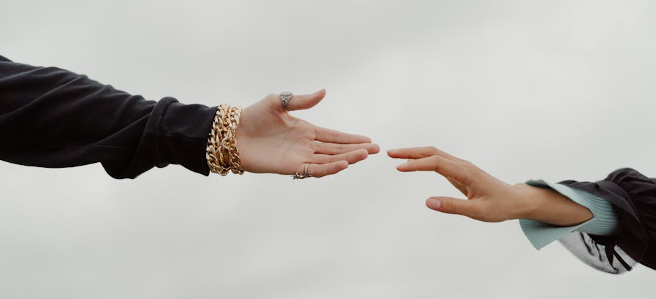 Eine Hand greift nach einer anderen Hand um ihr Hilfe anzubieten.