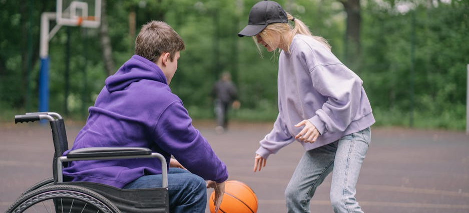 Ein Junge im Rollstuhl und ein Mädchen spielen gemeinsam Basketball auf dem Outdoor-Basketballplatz.