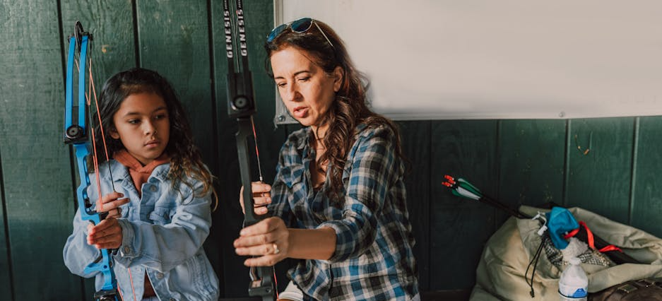 Frau erklärt Mädchen, auf was man bei der Nutzung einer Recurve-Sportbogens.