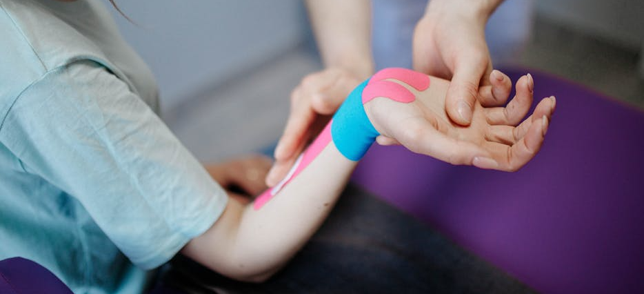 Eine Sporttherapeutin klebt Physiotape auf das Handgelenk einer Sportlerin, das bei der körpereigenen Heilung unterstützen soll.