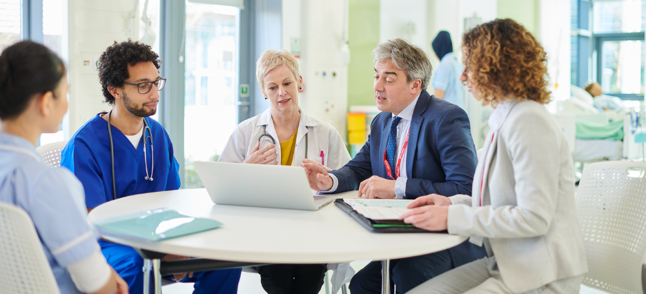 Eine Pflegeexpertin, eine Ärztin und noch weitere Mitglieder des Krankenhauspersonals sichten Untersagen und diskutieren angeregt. Eine Pflegeexpertin, eine Ärztin und noch weitere Mitglieder des Krankenhauspersonals sichten Untersagen und diskutieren angeregt.