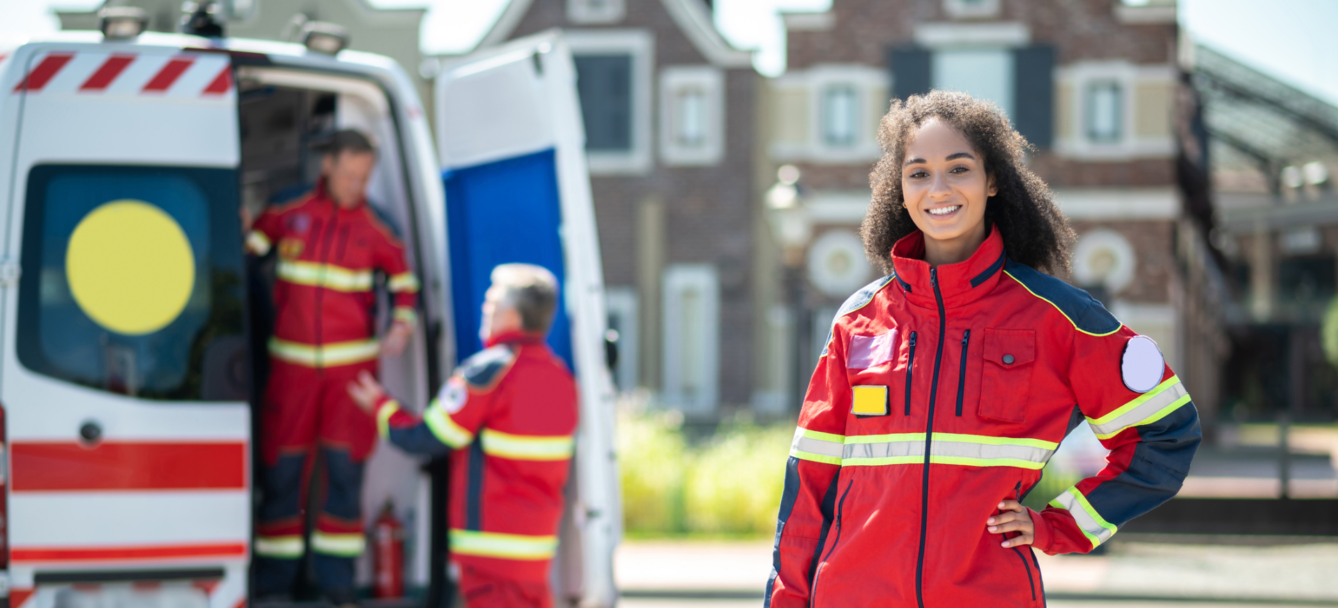 Rettungssanitäterin steht einsatzbereit in Arbeitskleidung vor dem Krankenwagen.